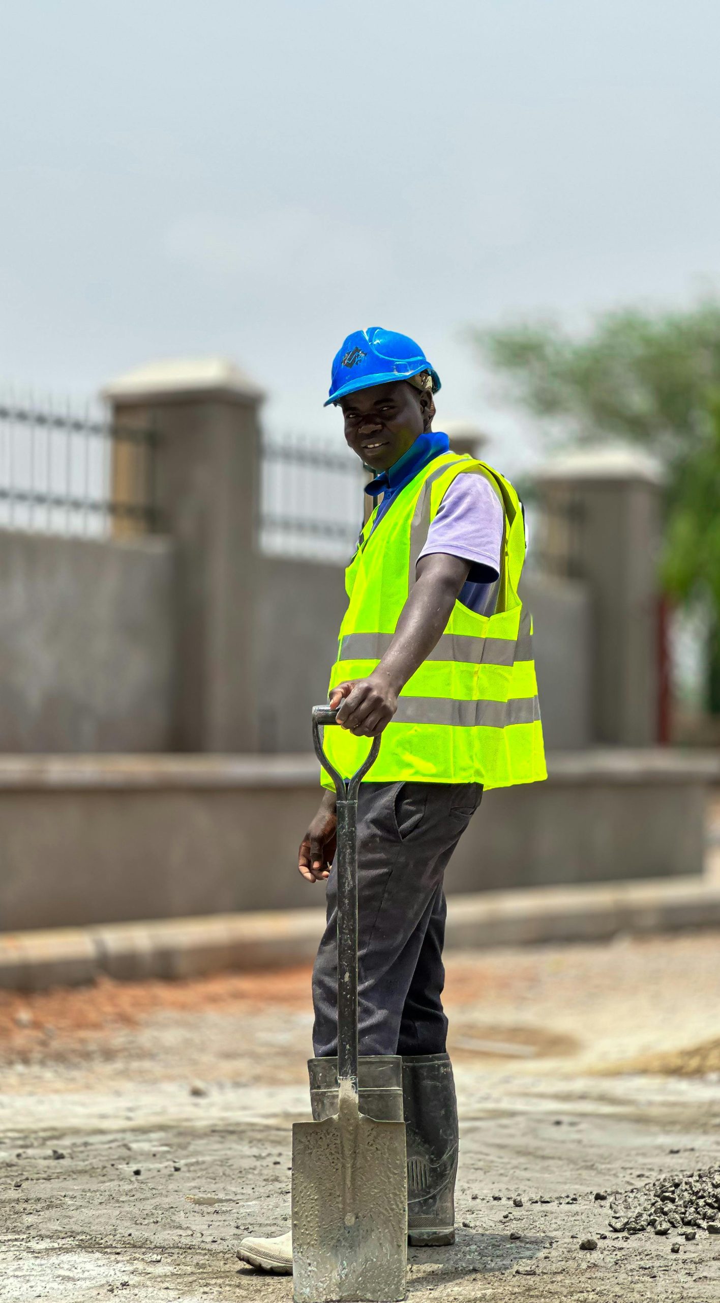 Outdoor scene of a construction worker with safety gear and shovel on a site.